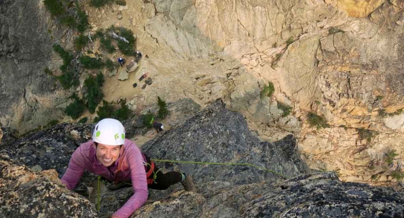 a person smiles while looking up as they climb up a rock wall